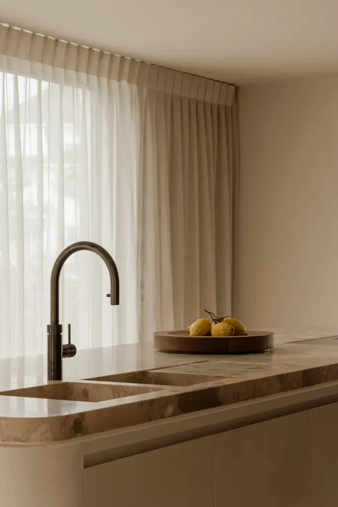 Natuurstenen kookeiland met zwarte kraan en een schaal met citroenen, Villarenovatie in Knokke, interieur Laura Calleeuw