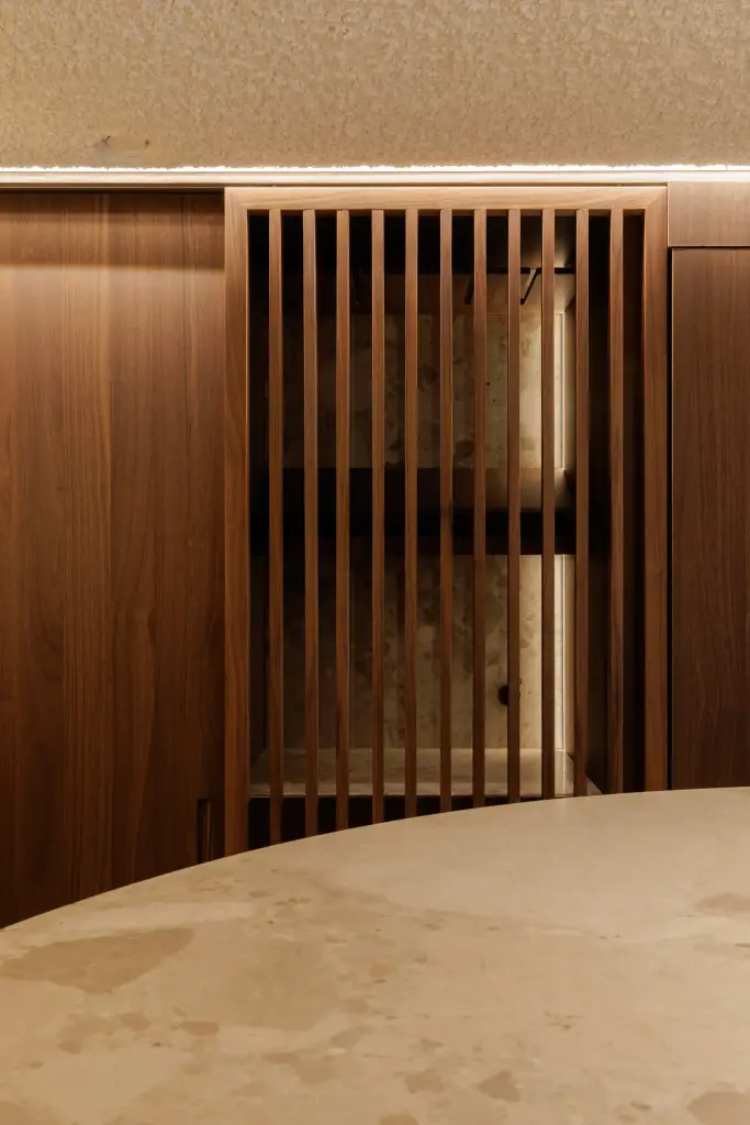 Lamellenkast in notelaar met ledverlichting boven de natuurstenen tafel, Villarenovatie in Knokke, interieur Laura Calleeuw