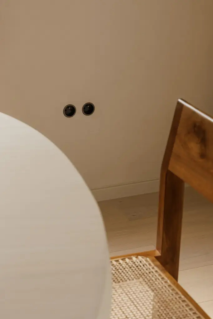 Detail van een rieten stoel naast een ronde witte tafel, Villarenovatie in Knokke, interieur Laura Calleeuw