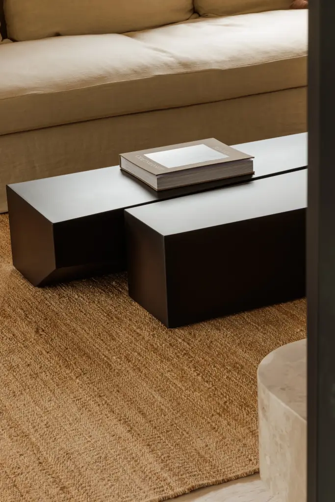 Twee zwarte salontafels met een boek op een jute tapijt voor de sofa, Villarenovatie in Knokke, interieur Laura Calleeuw