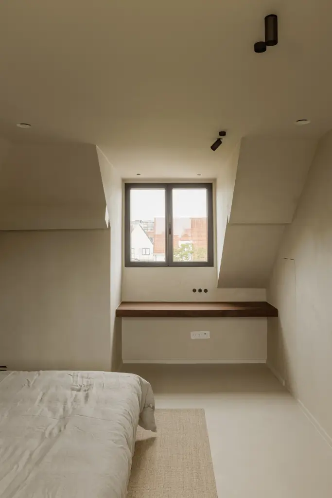 Slaapkamer onder de dakhelling met bed, zwevend bureau en een klein venster, Villarenovatie in Knokke, interieur Laura Calleeuw