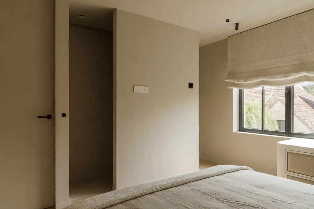 Slaapkamer met bed, deur en een raam met roman blind, Villarenovatie in Knokke, interieur Laura Calleeuw