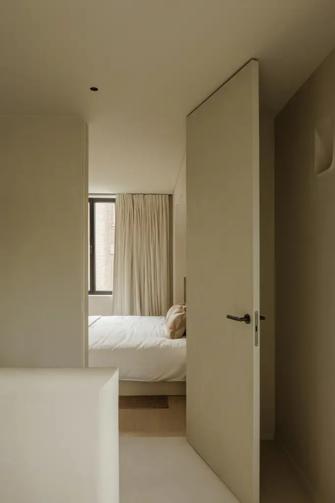 Open deur met doorkijk naar de slaapkamer met bed en gordijn, Villarenovatie in Knokke, interieur Laura Calleeuw