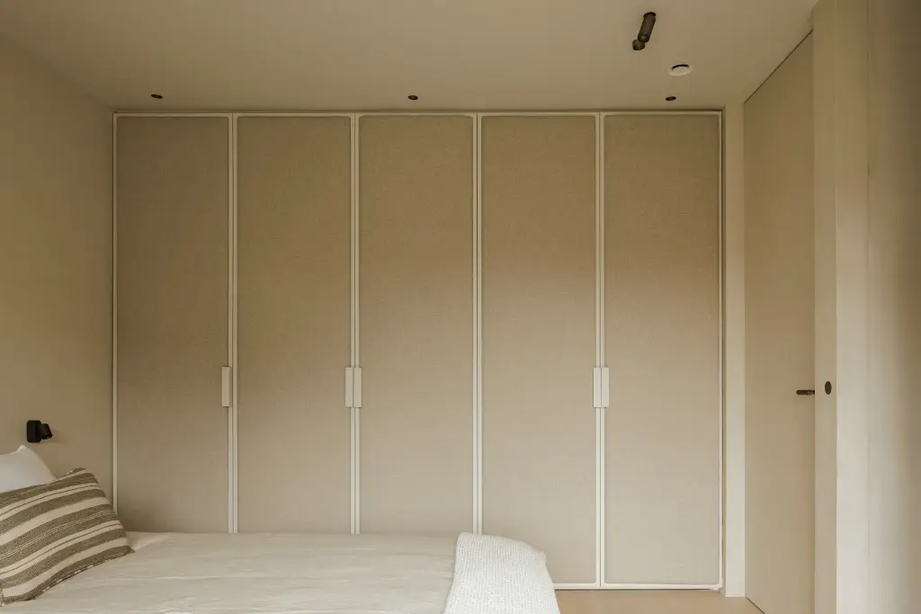 Slaapkamer met een kastenwand met ingefreesde grepen en een bed met gestreepte kussens, Villarenovatie in Knokke, interieur Laura Calleeuw