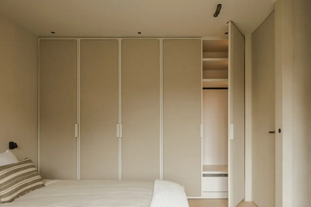 Slaapkamer met een kastenwand met ingefreesde grepen en een bed met gestreepte kussens, Villarenovatie in Knokke, interieur Laura Calleeuw