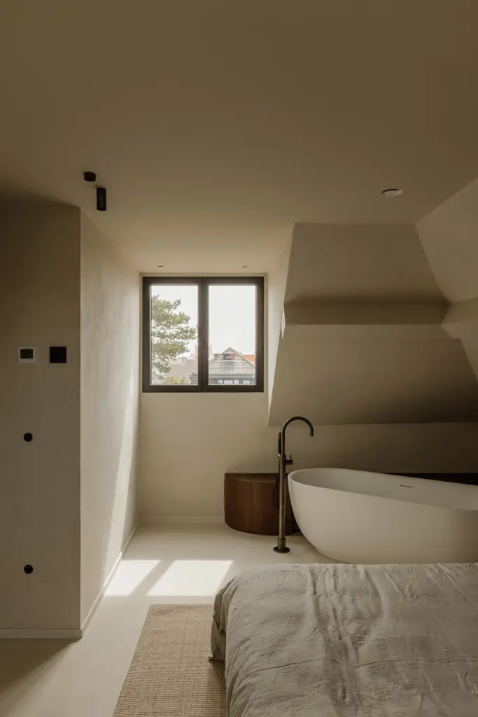 Slaapkamer met vrijstaand bad onder de dakhelling en een boogvormige doorgang, Villarenovatie in Knokke, interieur Laura Calleeuw
