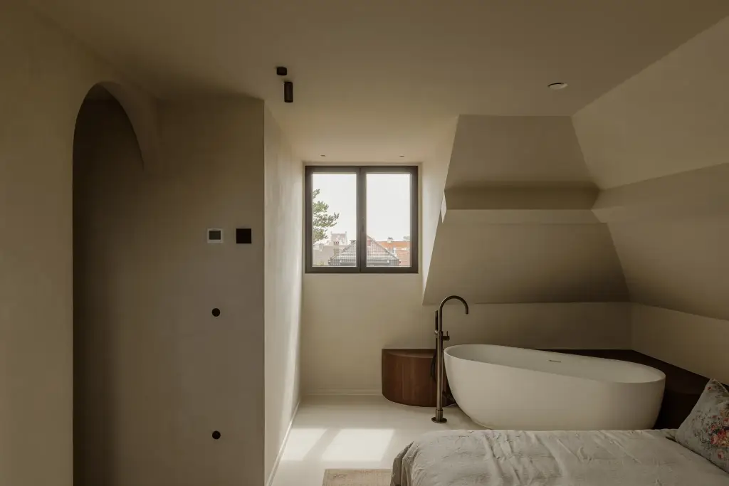 Slaapkamer met vrijstaand bad onder de dakhelling en een boogvormige doorgang, Villarenovatie in Knokke, interieur Laura Calleeuw