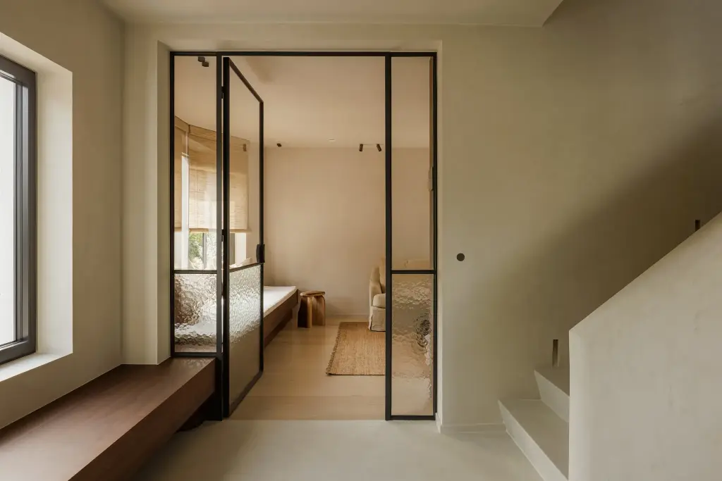 Stalen glaswand met zicht op een zitkamer met fauteuil en een bank in notelaar, Villarenovatie in Knokke, interieur Laura Calleeuw