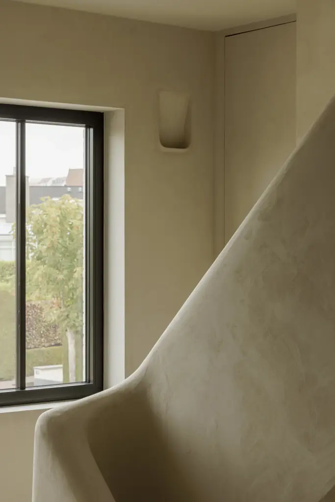 Gepleisterde trapleuning met een zwart raam op het trapportaal, Villarenovatie in Knokke, interieur Laura Calleeuw