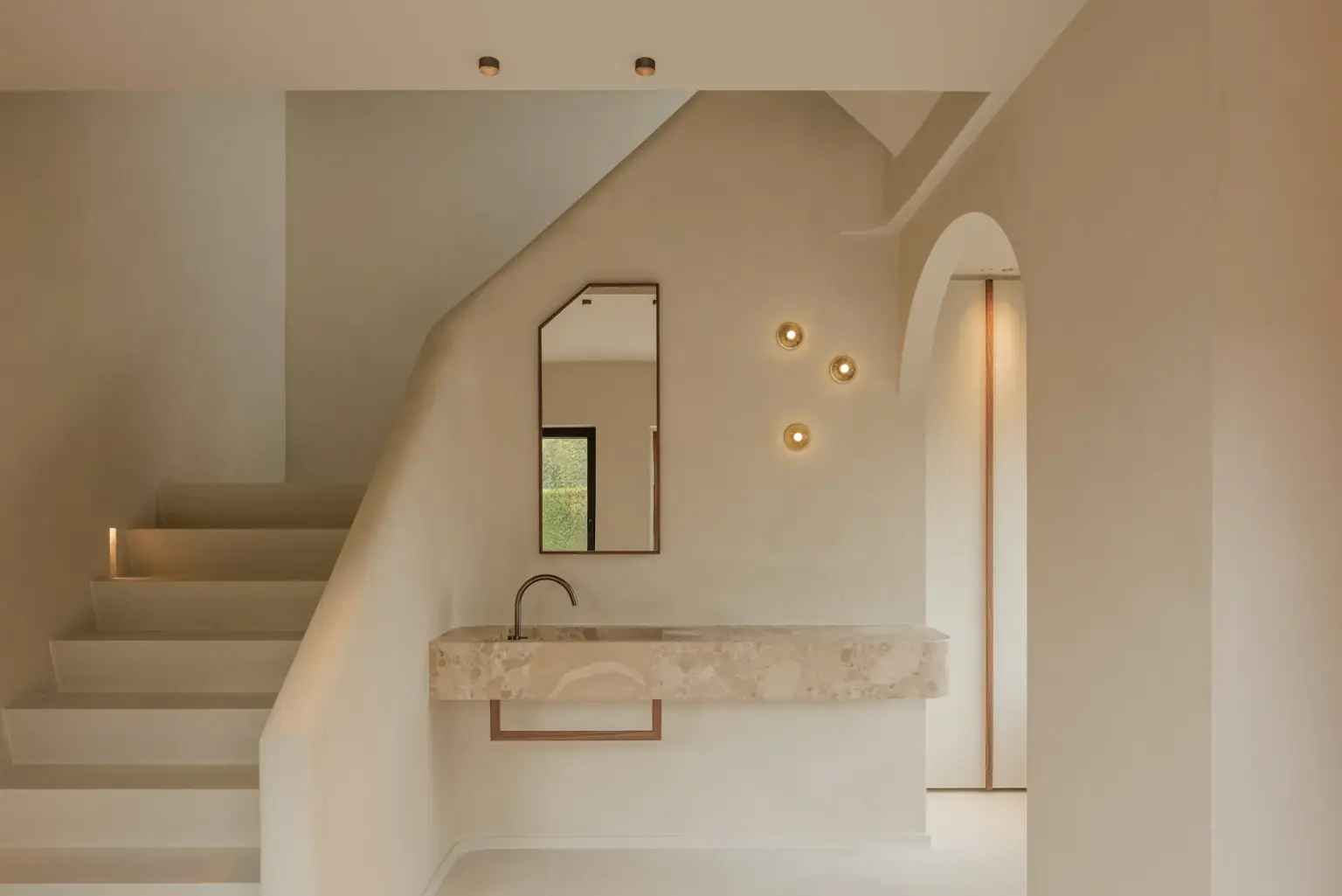 Trap in kalkpleister met zwevende natuurstenen wastafel, smalle spiegel en kleine wandlampjes, Villarenovatie in Knokke, interieur Laura Calleeuw