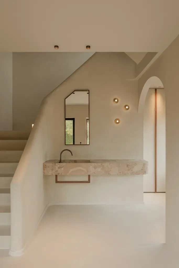 Trap in kalkpleister met zwevende natuurstenen wastafel, smalle spiegel en kleine wandlampjes, Villarenovatie in Knokke, interieur Laura Calleeuw