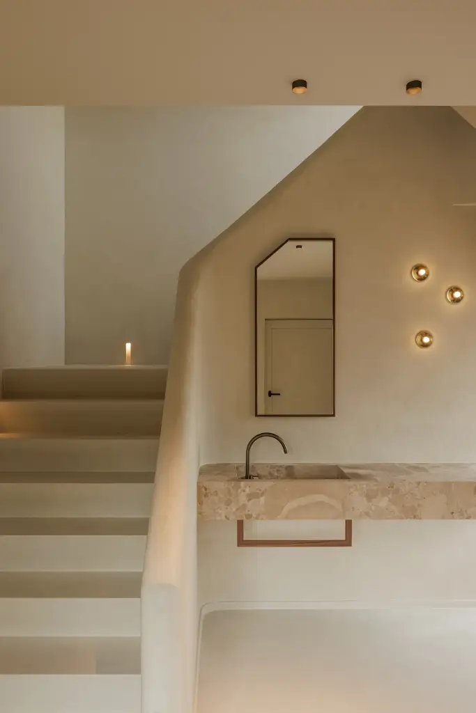 Trap in kalkpleister met zwevende natuurstenen wastafel, smalle spiegel en kleine wandlampjes, Villarenovatie in Knokke, interieur Laura Calleeuw