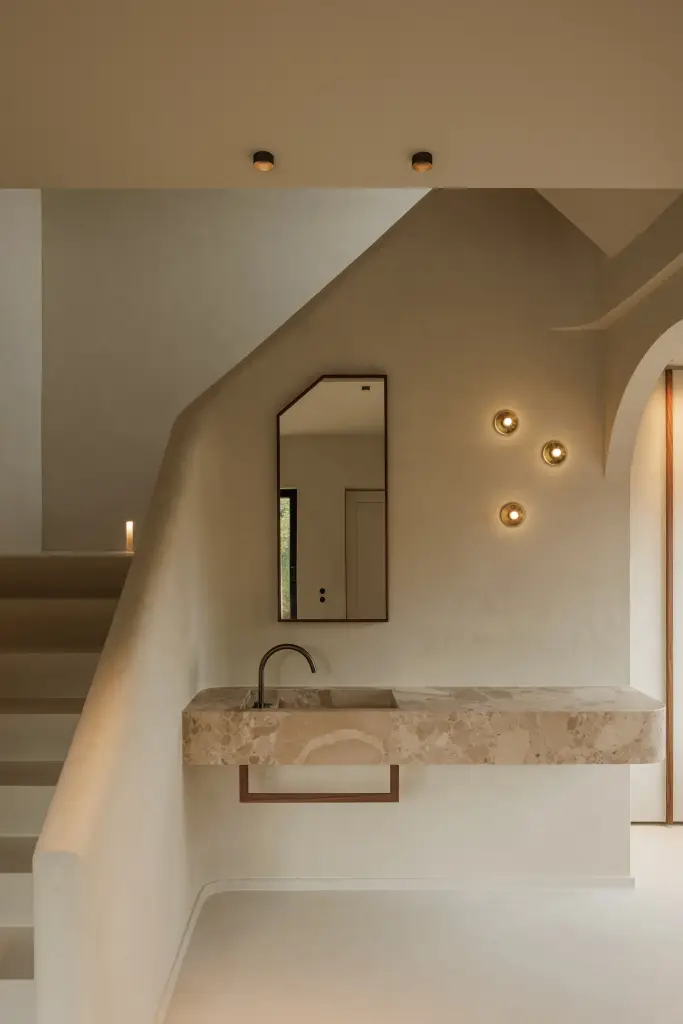 Trap in kalkpleister met zwevende natuurstenen wastafel, smalle spiegel en kleine wandlampjes, Villarenovatie in Knokke, interieur Laura Calleeuw