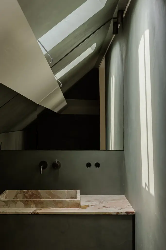 Natuurstenen wastafel met wandkraan en spiegel onder een dakvenster in een groene pleisterwand, Villarenovatie in Knokke, interieur Laura Calleeuw
