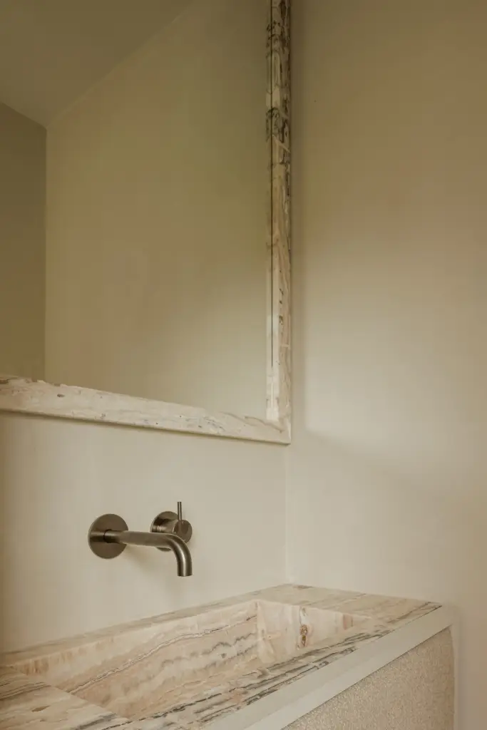 Gestreepte natuurstenen wastafel met wandkraan en een spiegel met oude lijst, Villarenovatie in Knokke, interieur Laura Calleeuw