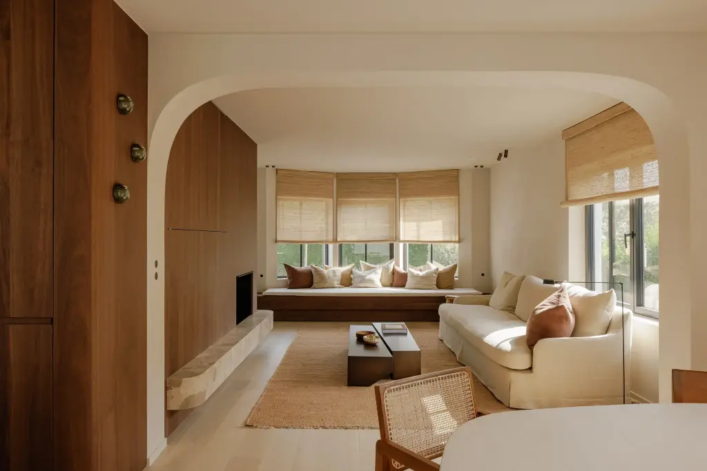 Leefruimte met boogopening, notelaren kastenwand, hoeksofa, rieten stoelen en roman blinds, Villarenovatie in Knokke, interieur Laura Calleeuw