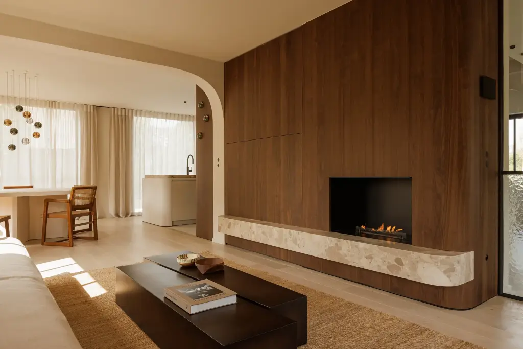 Leefruimte met open haard in een notelaren wand, natuurstenen rand, salontafel en eethoek op de achtergrond, Villarenovatie in Knokke, interieur Laura Calleeuw