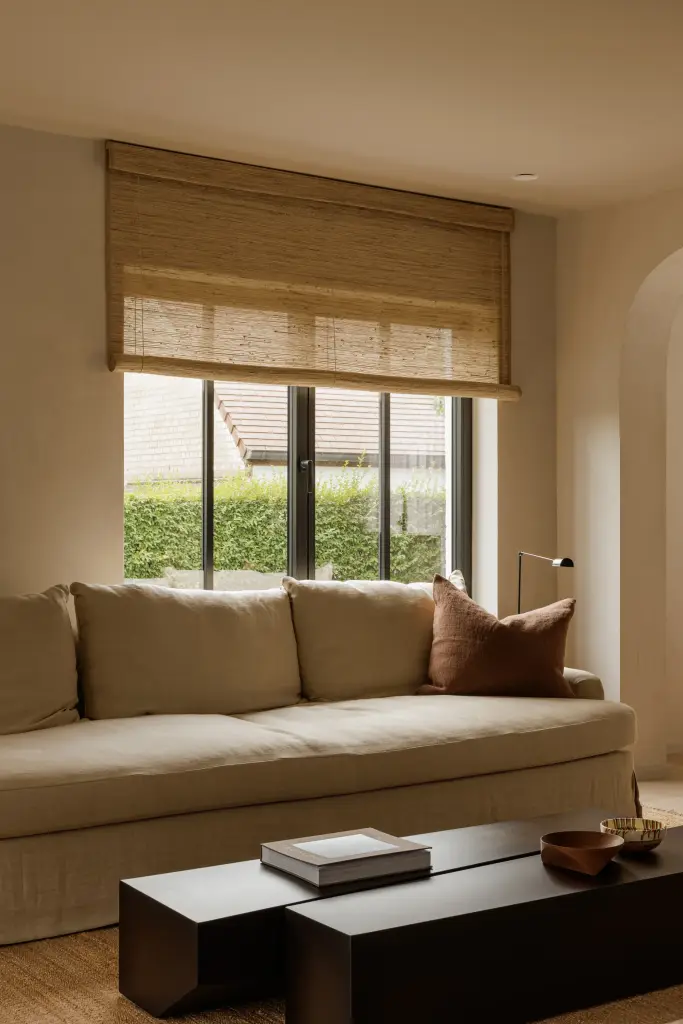Zithoek met sofa, zwarte salontafels en een raam met rieten roman blind, Villarenovatie in Knokke, interieur Laura Calleeuw