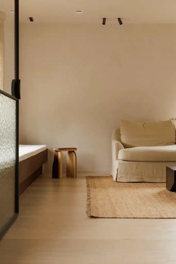 Zitkamer achter een stalen glaswand met fauteuil, bijzettafeltje en een jute tapijt, Villarenovatie in Knokke, interieur Laura Calleeuw
