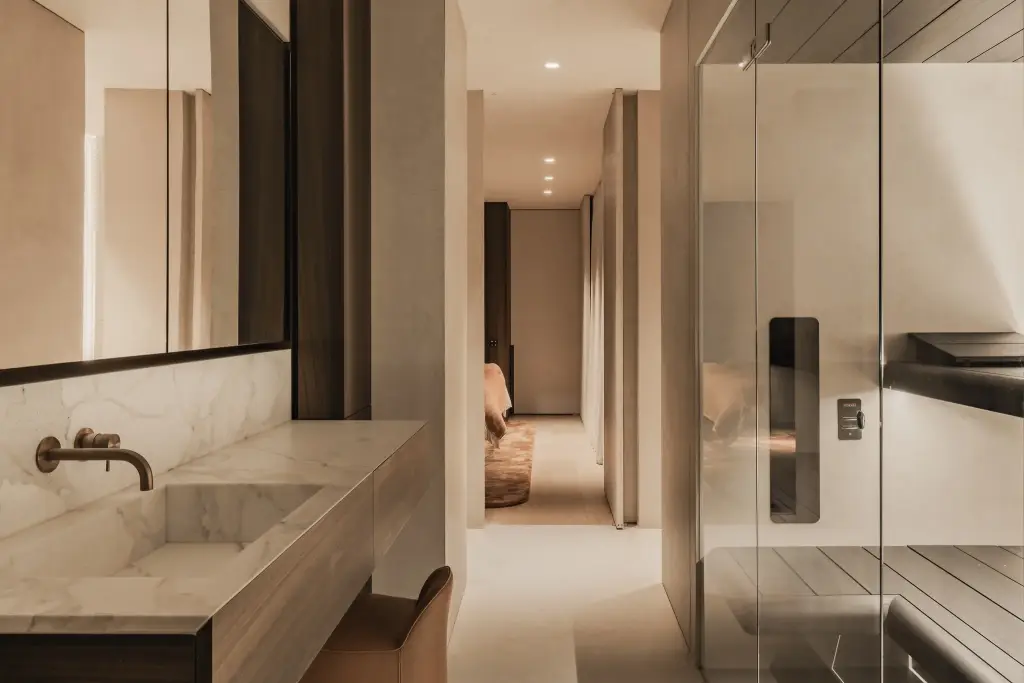 Marmeren wastafel met wandkraan, glaswand naar de sauna en doorkijk naar de slaapkamer, Penthouse in Kortrijk, interieur Laura Calleeuw