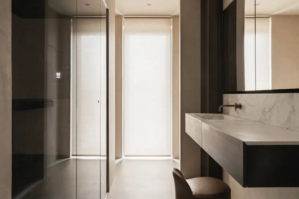Badkamer met zwevend donker houten wastafelmeubel, marmeren wand, glazen sauna en een leren stoel, Penthouse in Kortrijk, interieur Laura Calleeuw