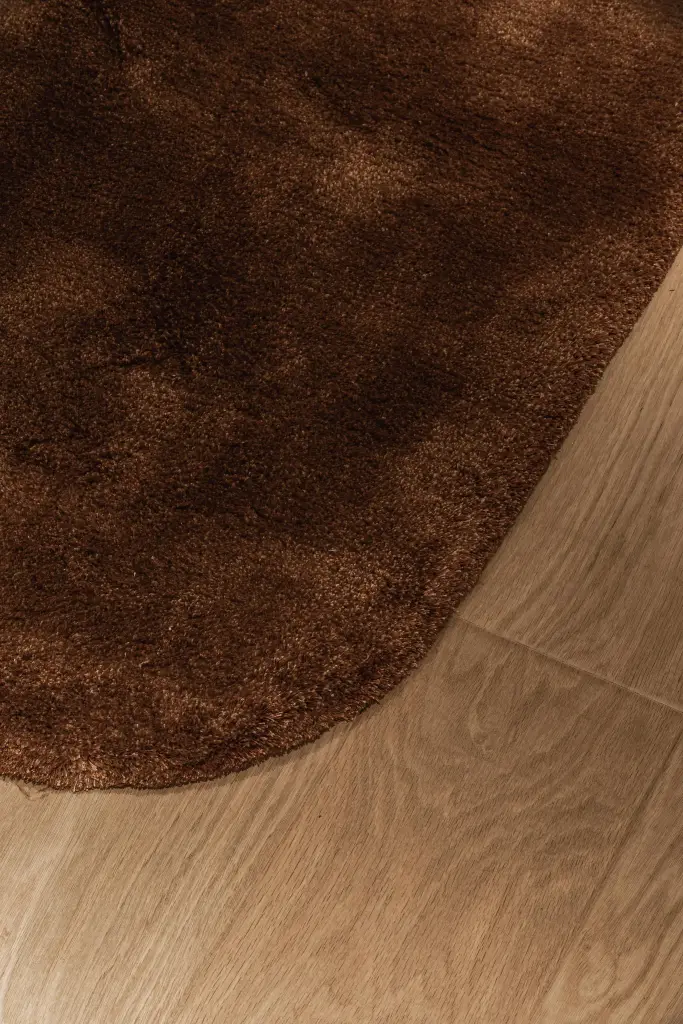 Detail van een bruin hoogpolig tapijt op eikenhouten parket, Penthouse in Kortrijk, interieur Laura Calleeuw