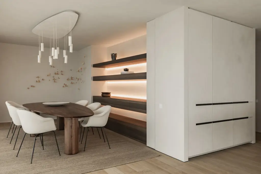 Eetkamer met ovale notelaren tafel, witte stoelen, hanglamp met witte buisjes en verlichte planken, Penthouse in Kortrijk, interieur Laura Calleeuw