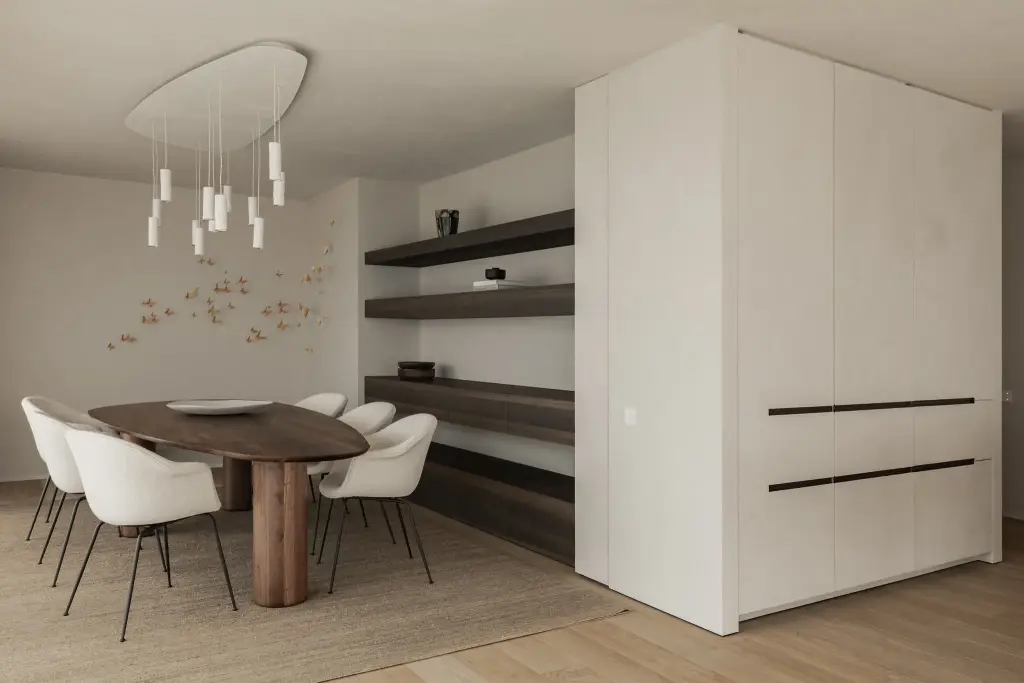 Eetkamer met ovale notelaren tafel, witte stoelen, hanglamp met witte buisjes en verlichte planken, Penthouse in Kortrijk, interieur Laura Calleeuw