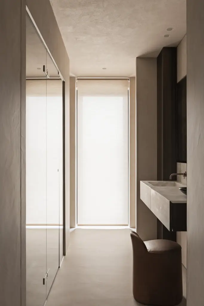 Gang naar de badkamer met een zwevende wastafel in donker hout, glaswand en een leren stoel, Penthouse in Kortrijk, interieur Laura Calleeuw