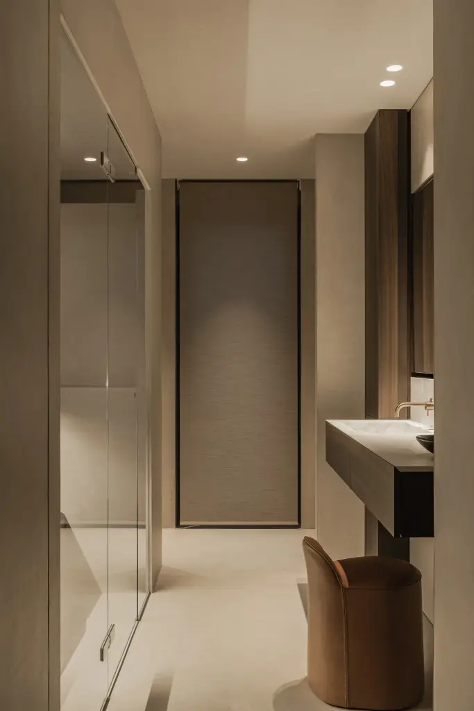 Gang naar de badkamer met een zwevende wastafel in donker hout, glaswand en een leren stoel, Penthouse in Kortrijk, interieur Laura Calleeuw