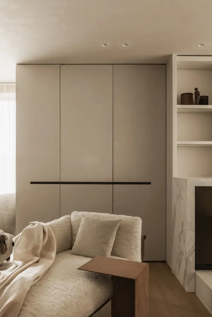 Kastenwand met verborgen inbouwovens en wijnkast, met een fauteuil met plaid op de voorgrond, Penthouse in Kortrijk, interieur Laura Calleeuw