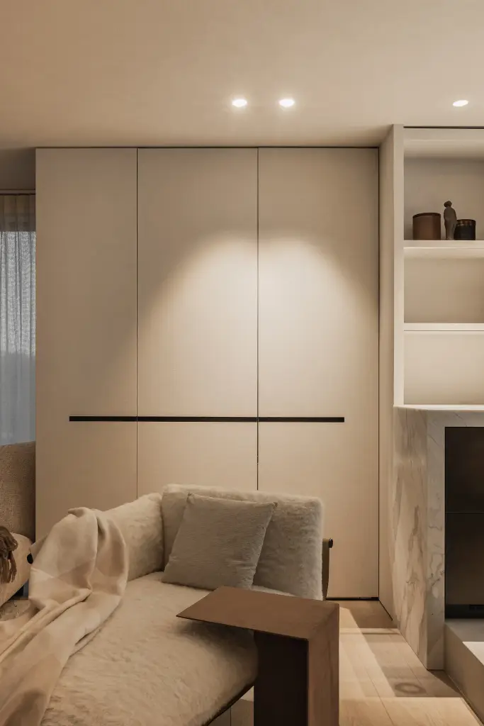 Kastenwand met verborgen inbouwovens en wijnkast, met een fauteuil met plaid op de voorgrond, Penthouse in Kortrijk, interieur Laura Calleeuw
