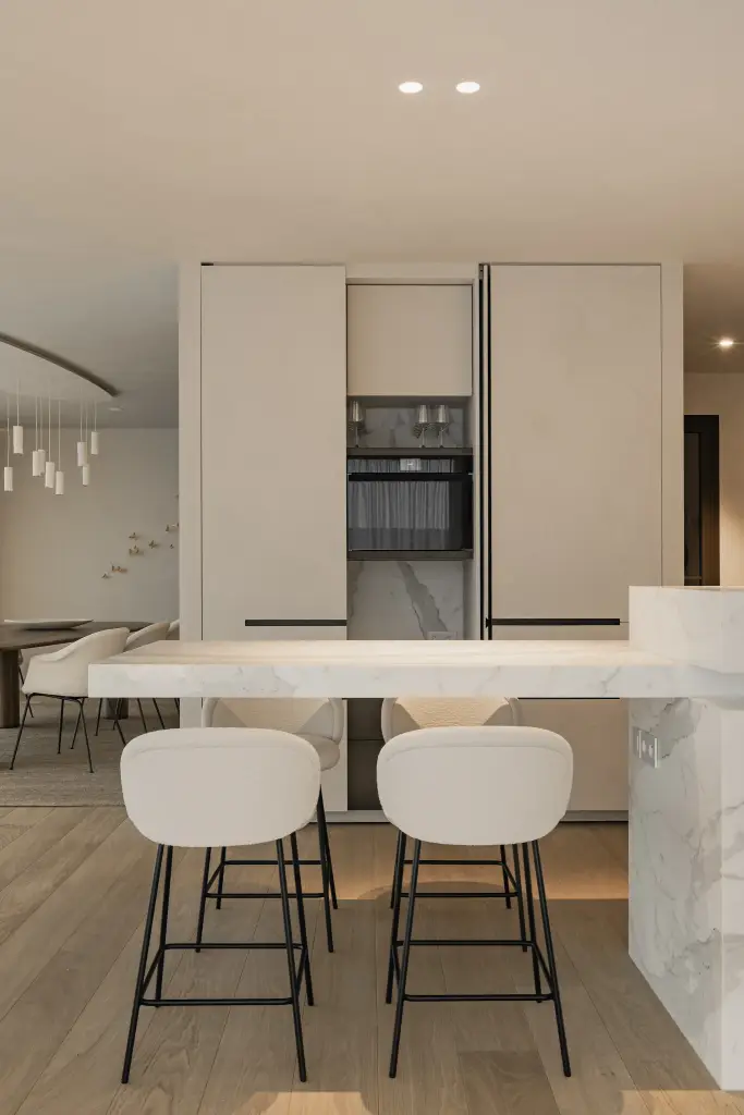 Keuken met witte kastenwand en inbouwoven, kookeiland in marmer met barkrukken, Penthouse in Kortrijk, interieur Laura Calleeuw