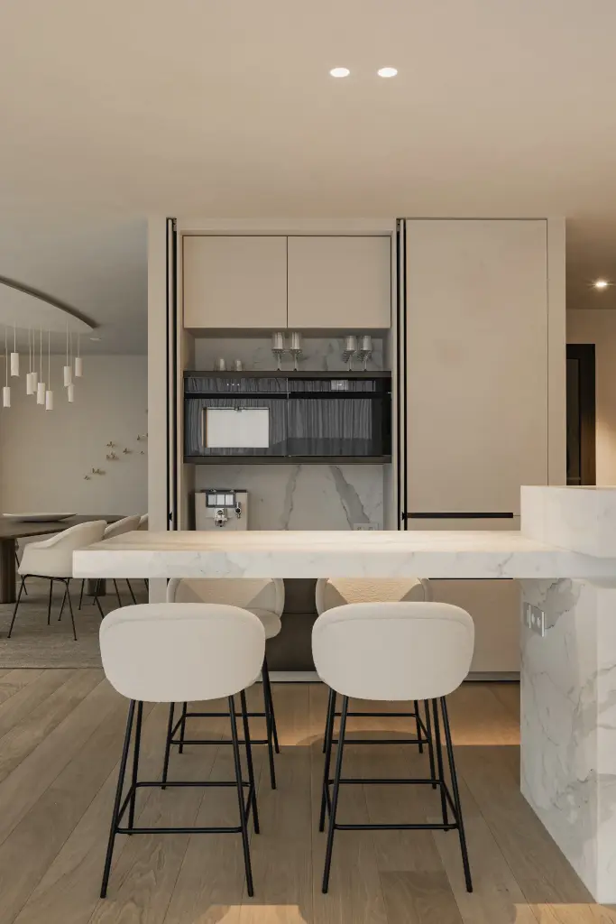 Keuken met witte kastenwand en inbouwoven, kookeiland in marmer met barkrukken, Penthouse in Kortrijk, interieur Laura Calleeuw