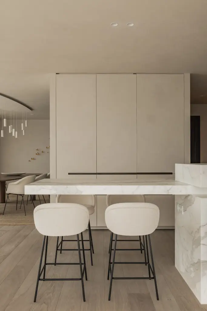 Witte keukenkasten met inbouwoven en marmeren eiland met witte barkrukken, Penthouse in Kortrijk, interieur Laura Calleeuw