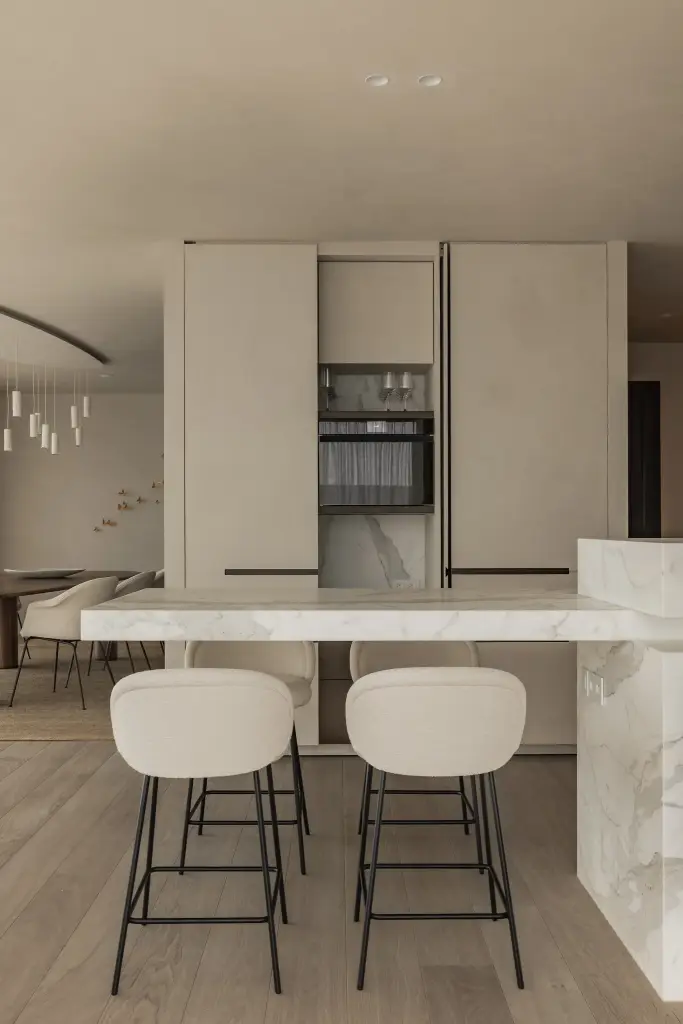 Witte keukenkasten met inbouwoven en marmeren eiland met witte barkrukken, Penthouse in Kortrijk, interieur Laura Calleeuw