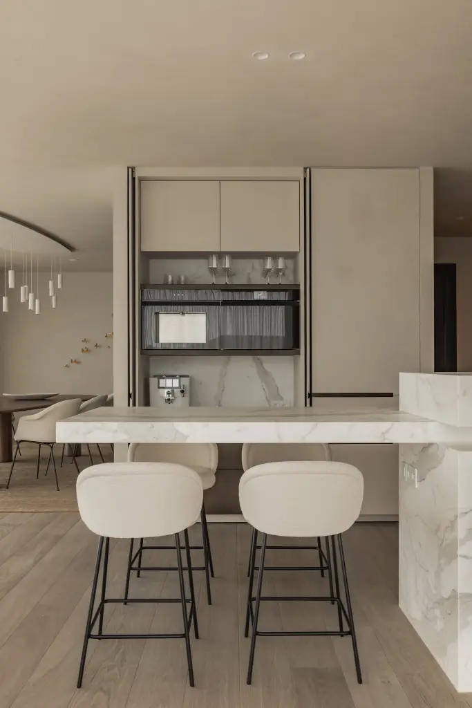 Witte keukenkasten met inbouwoven en marmeren eiland met witte barkrukken, Penthouse in Kortrijk, interieur Laura Calleeuw
