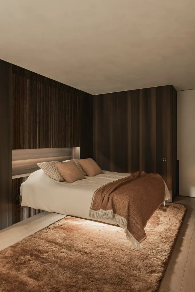 Slaapkamer met notelaren wanden, bed met terracotta plaid en een tapijt met verlichting onder het bed, Penthouse in Kortrijk, interieur Laura Calleeuw