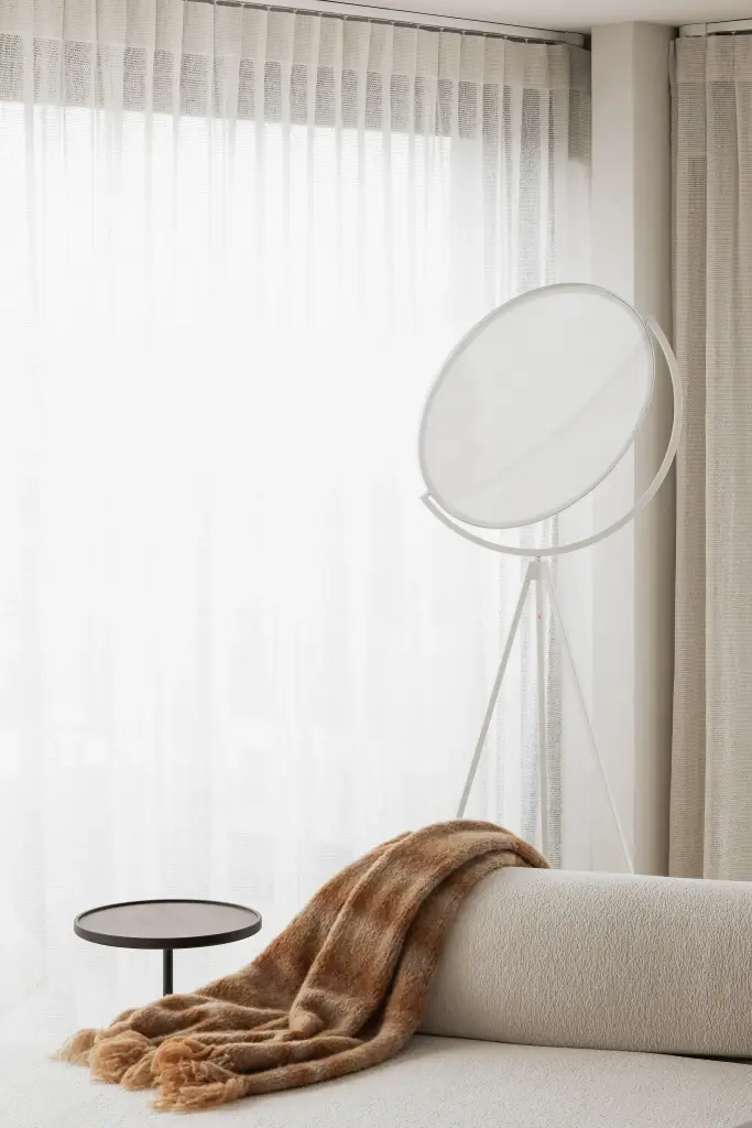 Ronde staande lamp, sofa met plaid en een bijzettafeltje voor een raam met vitrage, Penthouse in Kortrijk, interieur Laura Calleeuw