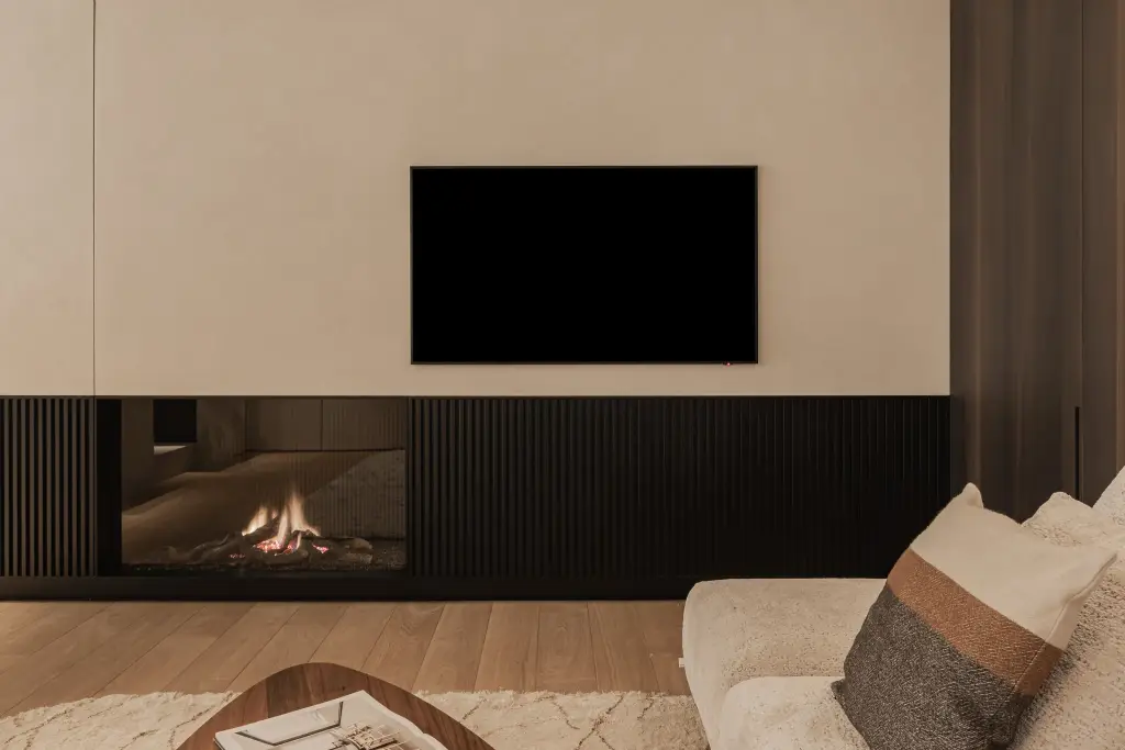 Televisie boven de open haard met zwarte lamellen en een kussen met bruine band, Penthouse in Kortrijk, interieur Laura Calleeuw