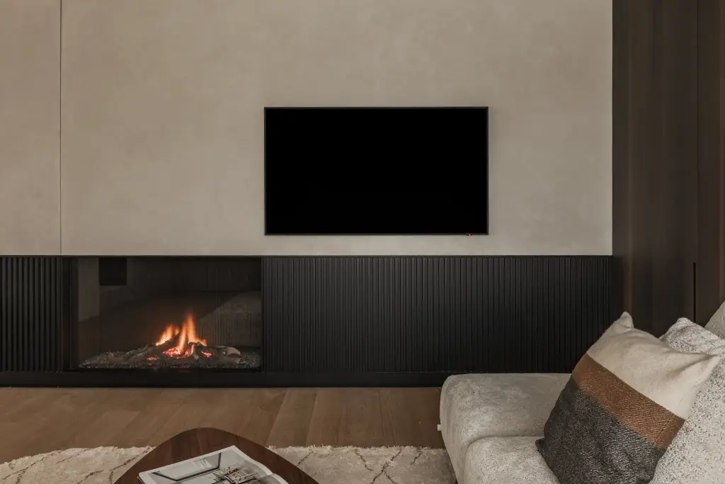 Televisie boven de open haard met zwarte lamellen en een kussen met bruine band, Penthouse in Kortrijk, interieur Laura Calleeuw