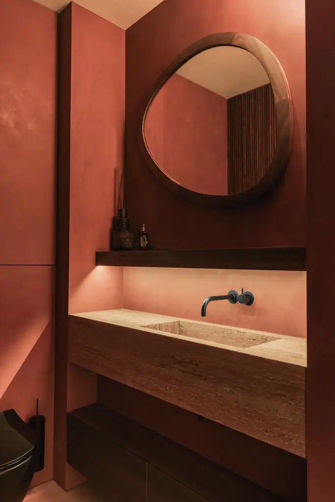 Toilet met ronde spiegel in notelaar, zwarte wandkraan en natuurstenen wastafel tegen een rode wand, Penthouse in Kortrijk, interieur Laura Calleeuw