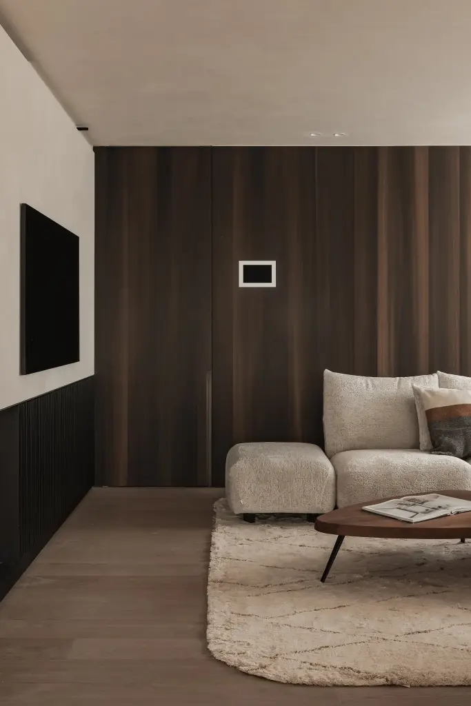 Leefruimte met notelaren wand, sofa en salontafel op een wollen tapijt met doorkijk naar de gang, Penthouse in Kortrijk, interieur Laura Calleeuw