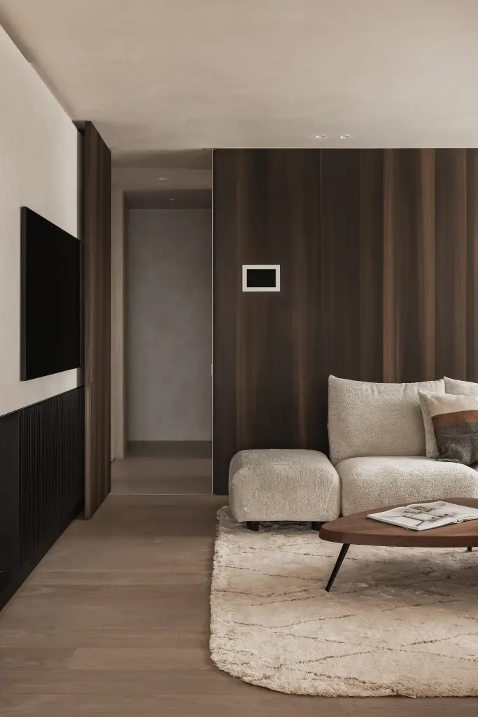 Leefruimte met notelaren wand, sofa en salontafel op een wollen tapijt met doorkijk naar de gang, Penthouse in Kortrijk, interieur Laura Calleeuw