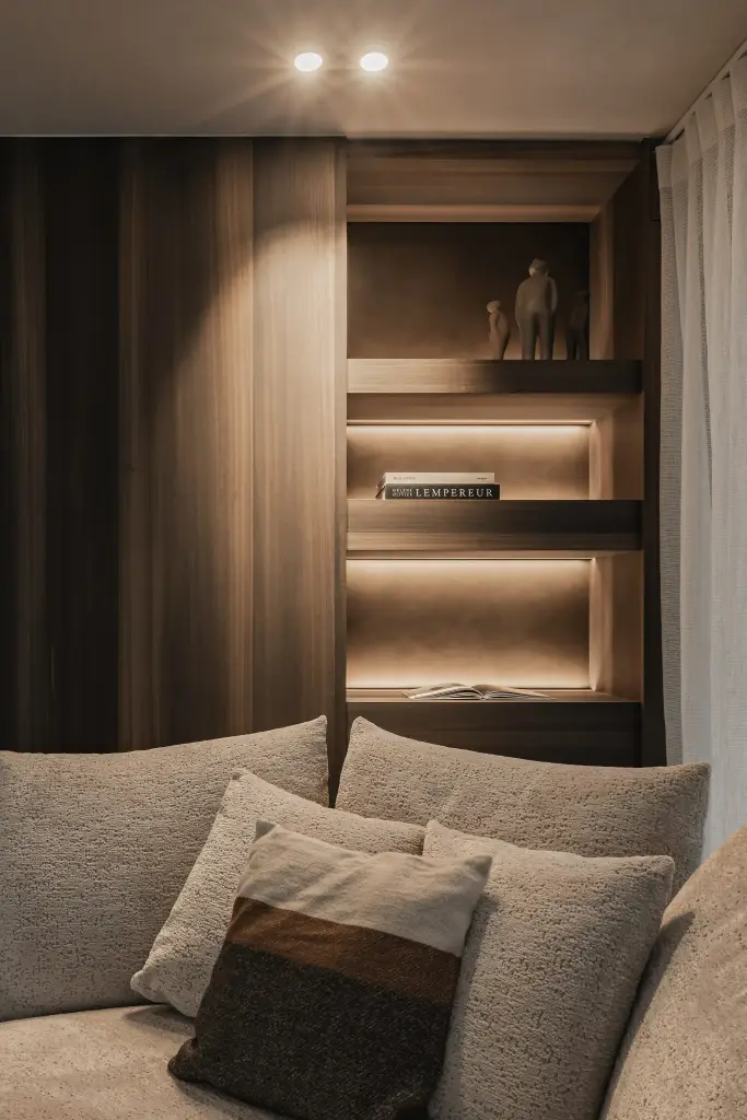 Sofa met kussens voor een notelaren kast met indirect licht, Penthouse in Kortrijk, interieur Laura Calleeuw