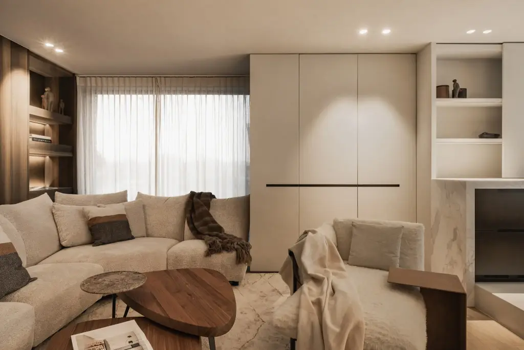 Zithoek met hoeksofa, notelaren salontafel en fauteuil voor een kastenwand met verborgen inbouwoven, Penthouse in Kortrijk, interieur Laura Calleeuw