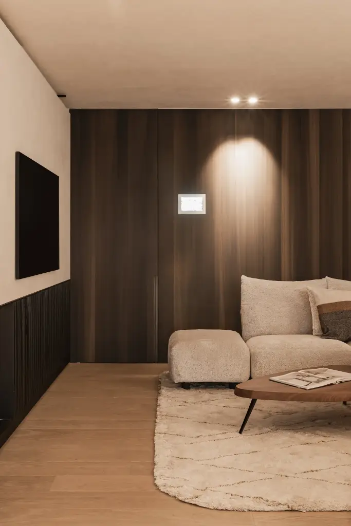 Zithoek voor een notelaren wand met spot en bedieningspaneel, met doorkijk naar de gang, Penthouse in Kortrijk, interieur Laura Calleeuw