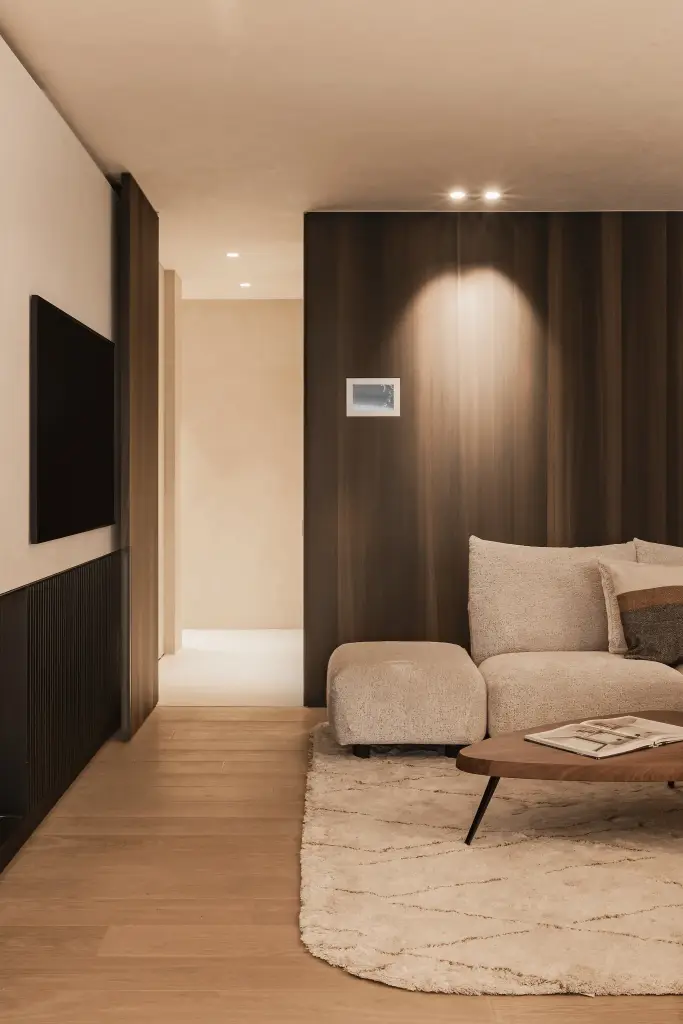 Zithoek voor een notelaren wand met spot en bedieningspaneel, met doorkijk naar de gang, Penthouse in Kortrijk, interieur Laura Calleeuw