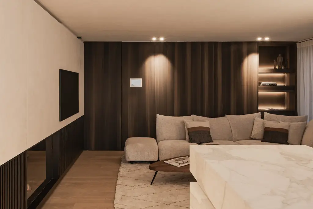 Zithoek met sofa voor een notelaren wand met televisie en spots, het marmeren eiland op de voorgrond, Penthouse in Kortrijk, interieur Laura Calleeuw