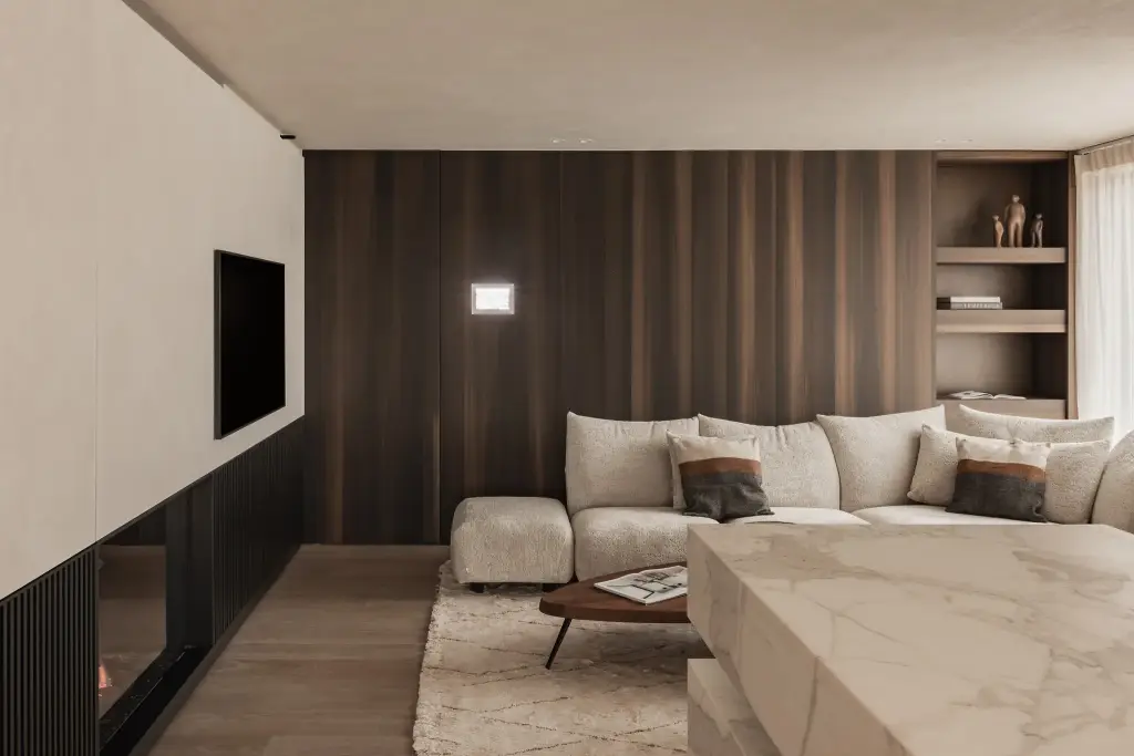 Zithoek met sofa voor een notelaren wand met televisie en spots, het marmeren eiland op de voorgrond, Penthouse in Kortrijk, interieur Laura Calleeuw